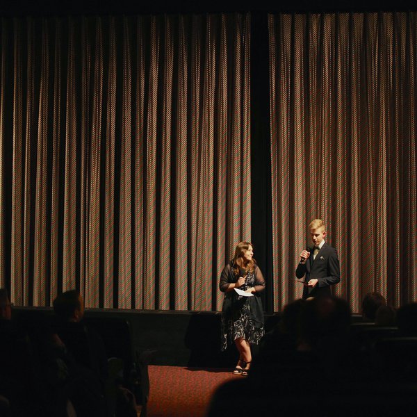 Zwei Personen vor einem geschlossenen Bühnenvorhang