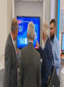 Vier Männer stehen, mit dem Rücken zur Kamera, neugierig vor einem Monitor.