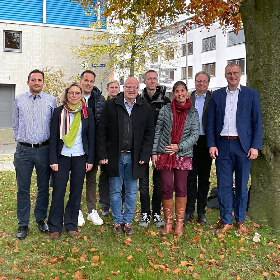 Auf dem Bild sind 31 Personen zu sehen, die als Gruppe im Halbkreis stehen. Sie sind business casual gekleidet und lächeln in die Kamera. 