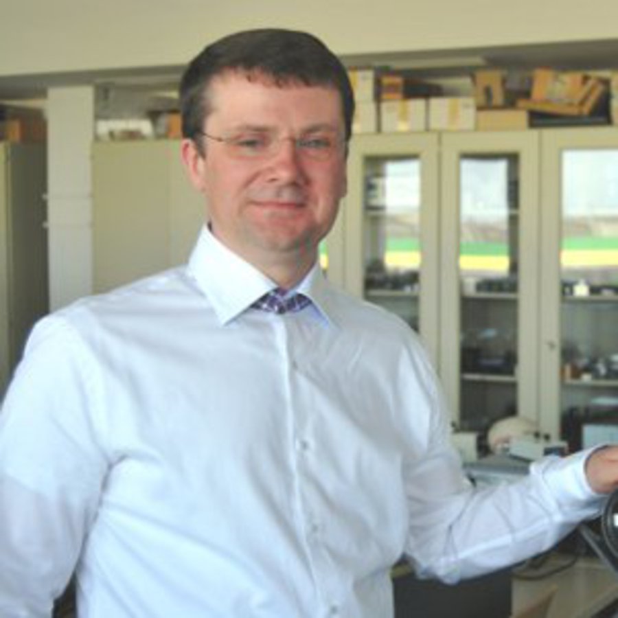 Ein Mann in einem weißen Hemd, steht in seinem Labor und lächelt freundlich in die Kamera.