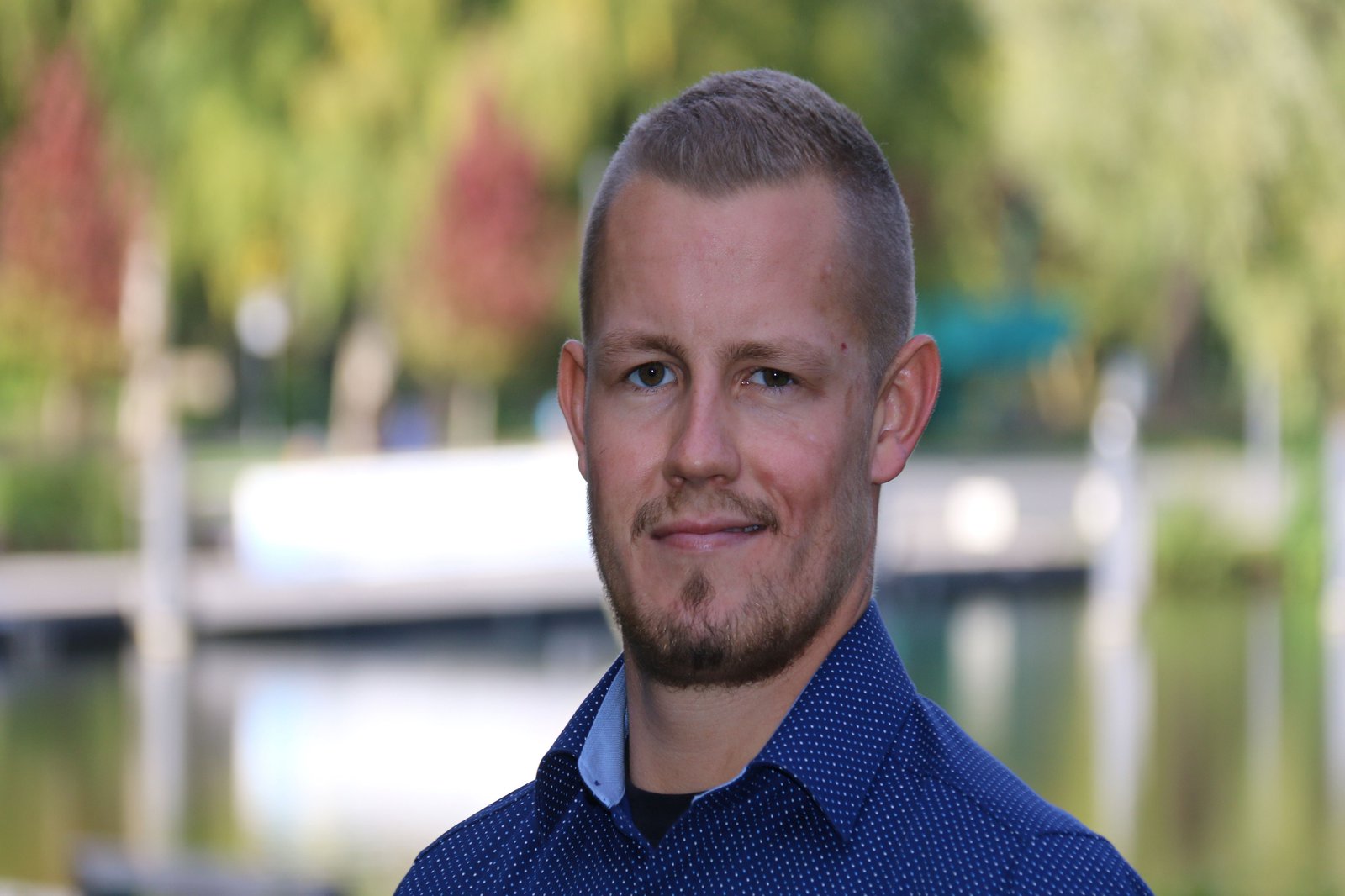 Ein Mann posiert im Freien und grinst in die Kamera.