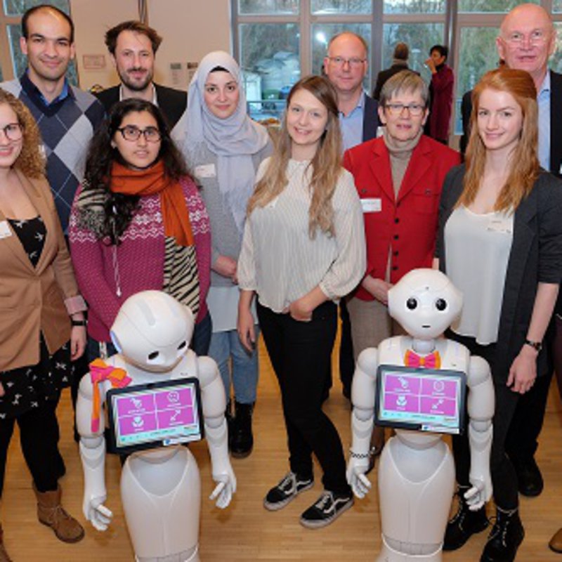 Gruppenbild mit Roboetrn: Forscherinnen und Forscher der FH Kiel und der Uni Siegen mit ihren Pepper-Robotern 