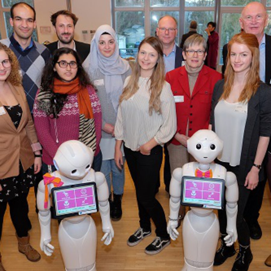 Gruppenbild mit Roboetrn: Forscherinnen und Forscher der FH Kiel und der Uni Siegen mit ihren Pepper-Robotern 