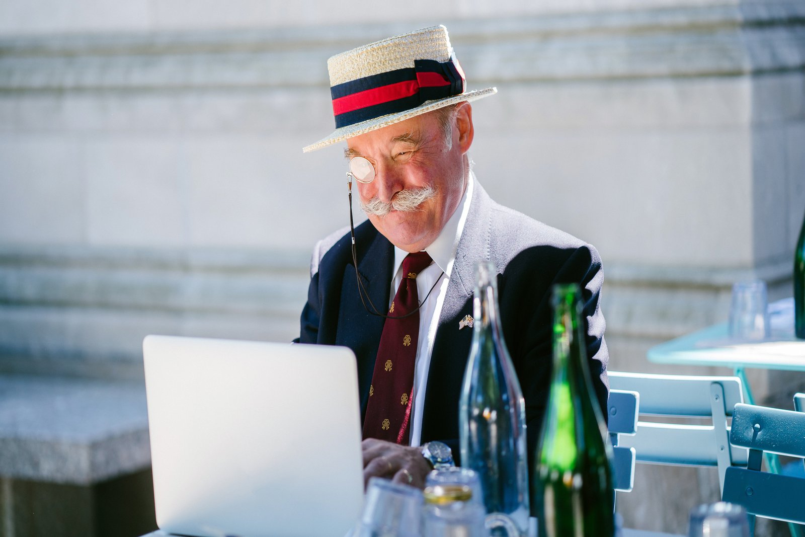 Ein sehr gut gekleideter älterer Mann sitz draussen im Halbschatten an seinem Laptop.