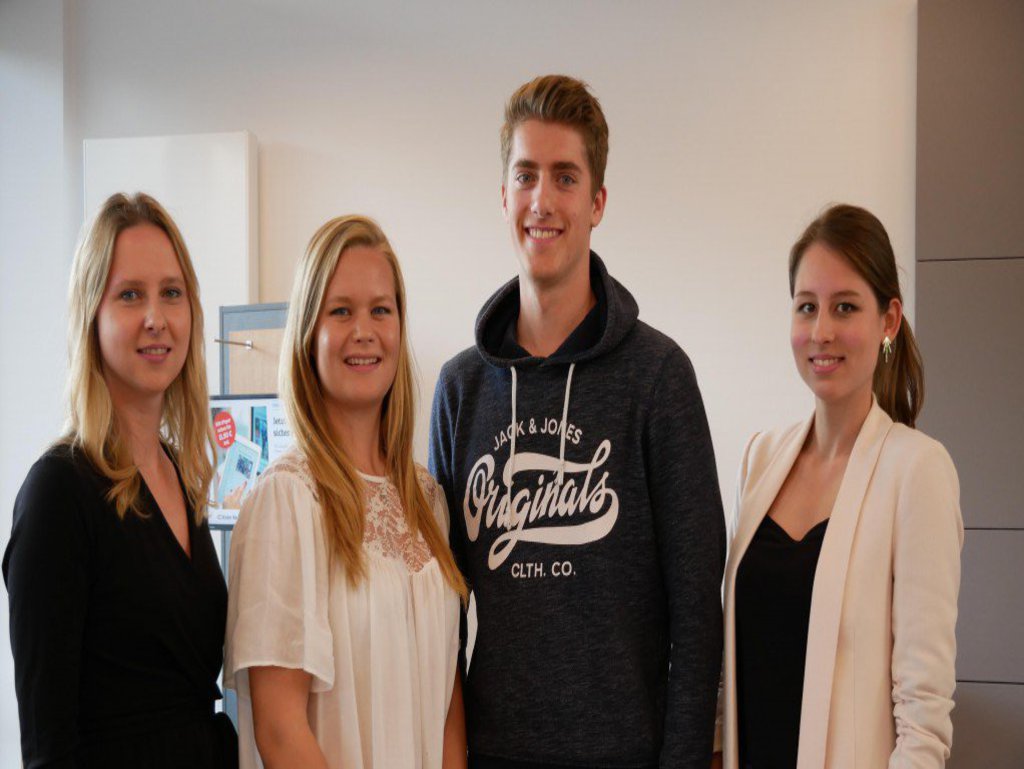 Drei Frauen und ein Mann posieren und lächeln freundlich in die Kamera.