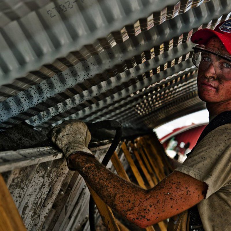 Ein Mann mit roter Cap und Schutzbrille steht mit dreckigen Armen unter einem Verschlag und hebt eine Leiter.