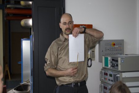 Ein Mann in seidig braunem Hemd demonstriert einen Vorgang.