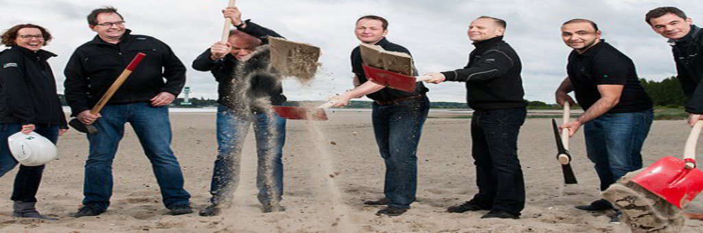 Eine Gruppe Menschen wirft Strandsand mit ihren Schaufeln hoch.