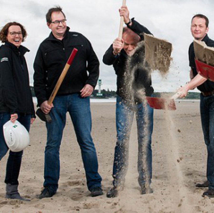 Eine Gruppe Menschen wirft Strandsand mit ihren Schaufeln hoch.