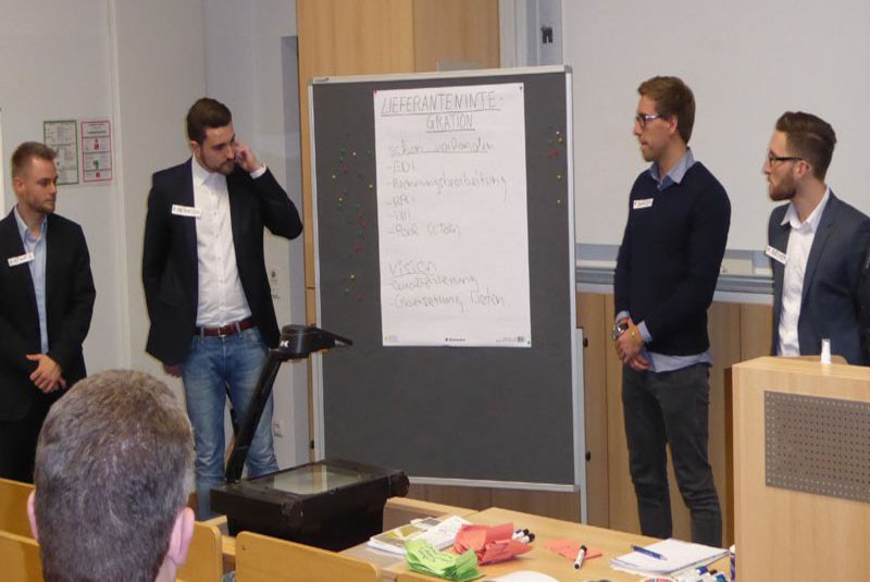 Vier Studenten positionieren sich seitlich von einer Pinnwand.