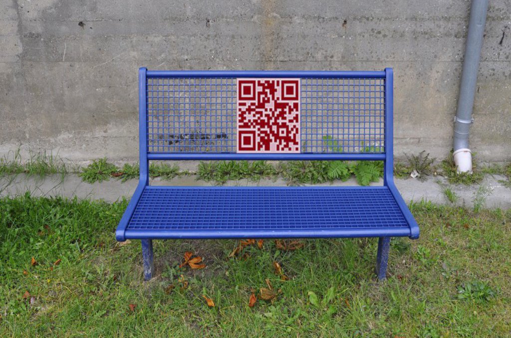 Eine blaue Bank steht auf einem grünen Stück Rasen. Auf ihr befindet sich ein großer roter Barcode.
