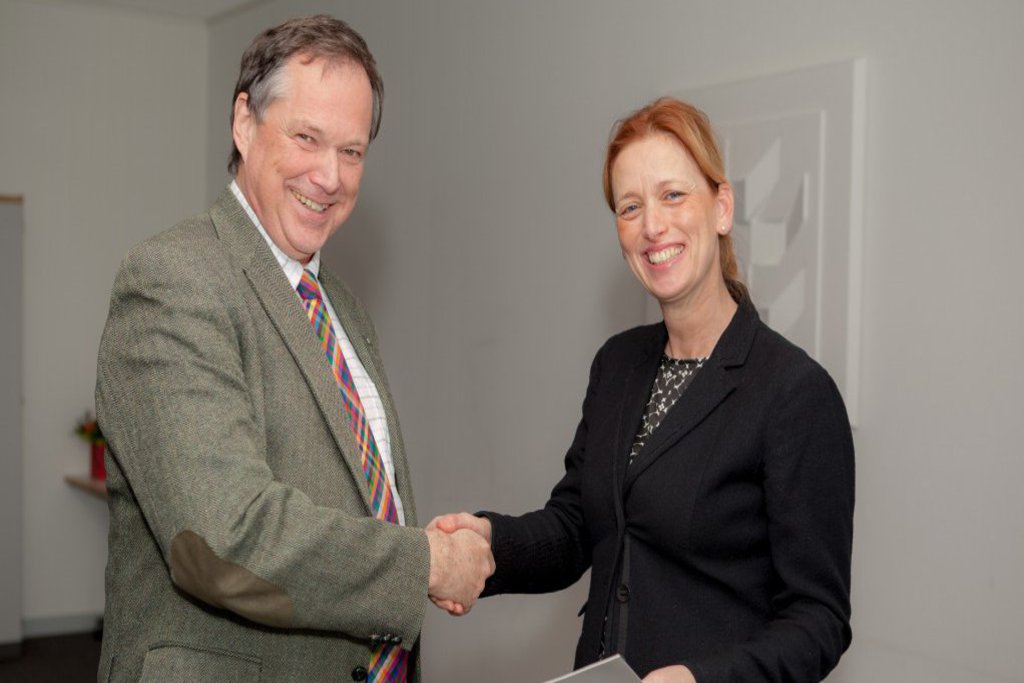 Eine Frau und ein Mann reichen sich die Hände und lächeln freundlich in die Kamera.