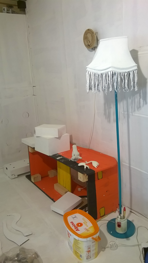 Ein Kinderauto aus Holz, steht wie ein Regal neben einer weißen Stehlampe.