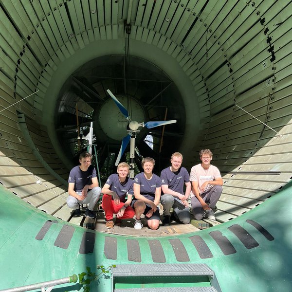 5 Studierende hocken vor einem großen Rotor