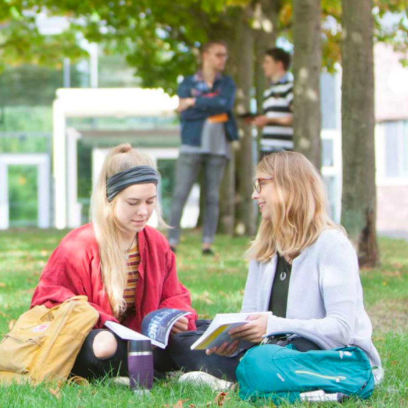Zwei Studentinnen sitzen auf einer Wiese, daneben in Textform: FIT für die Zukunft.