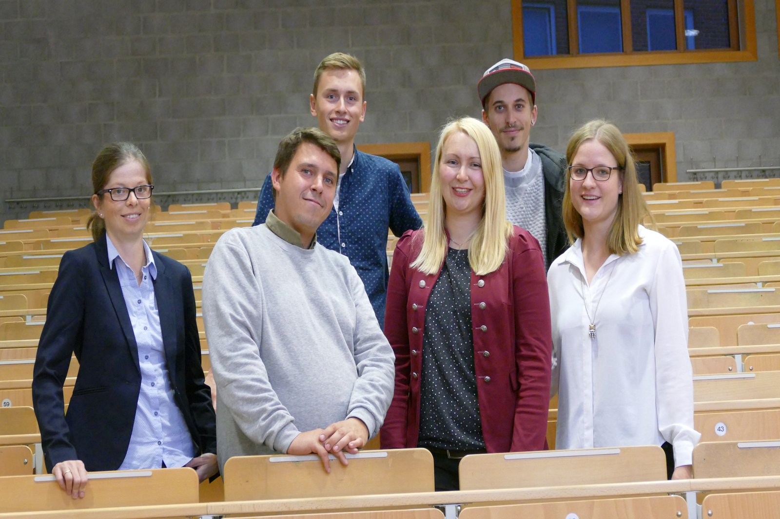 Eine Gruppe Studierender posiert in einem leeren Hörsaal.