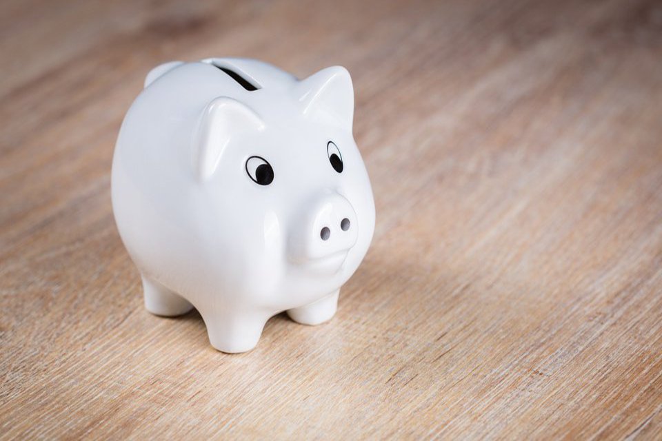 Ein weißes Sparschwein steht auf einem Holztisch.