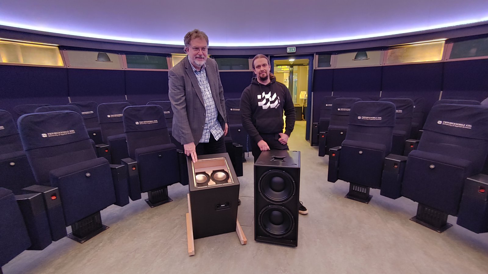 Zwei Männer im Mediendom der FH Kiel, vor ihnen stehen Subwoofer