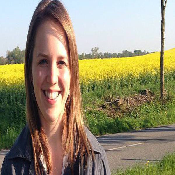 Eine Frau posiert vor einem Rapsfeld und lächelt in die Kamera.