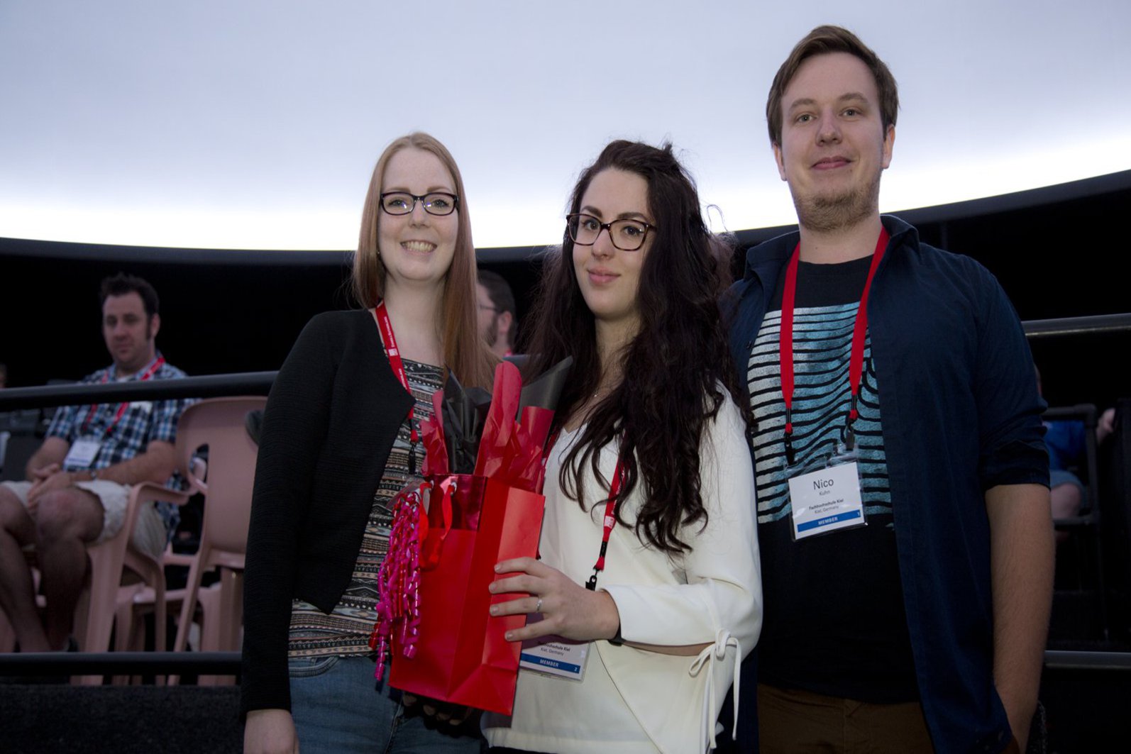 drei Studierende posieren und halten eine Geschenktüte in den Händen.