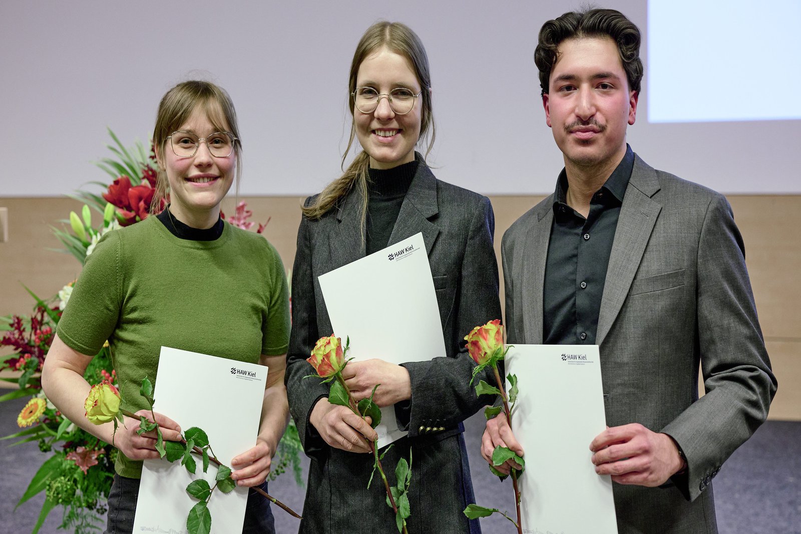 Drei Personen mit Urkunden in der Hand.