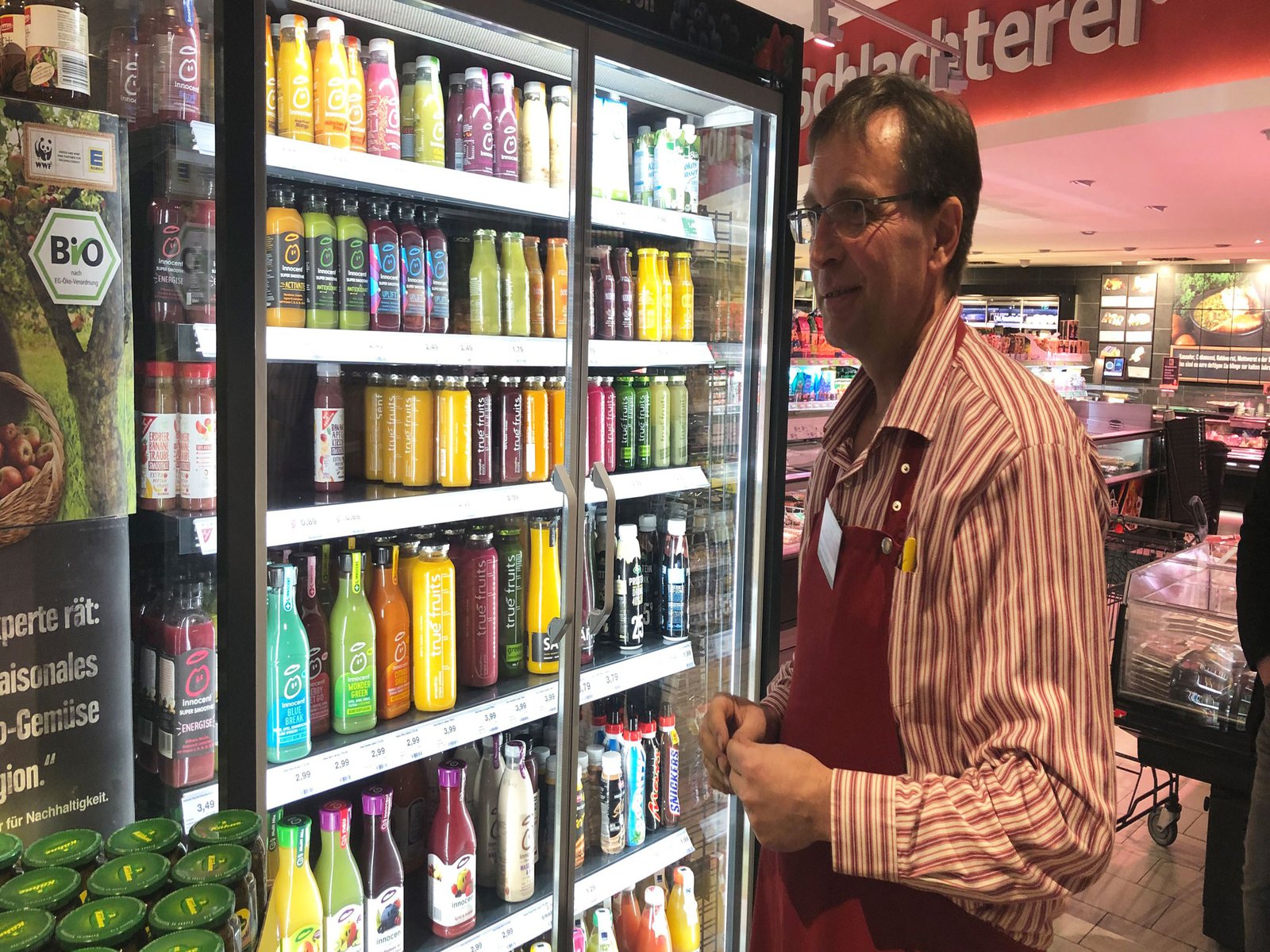 Ein Verkäufer vor einem Getränkekühlschrank mit Glastüren.