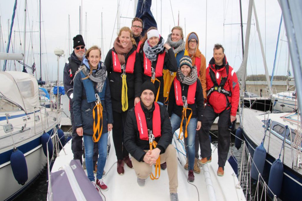 Eine Gruppe Segler:innen steht am Bug eines Segelboots und posiert für die Kamera.