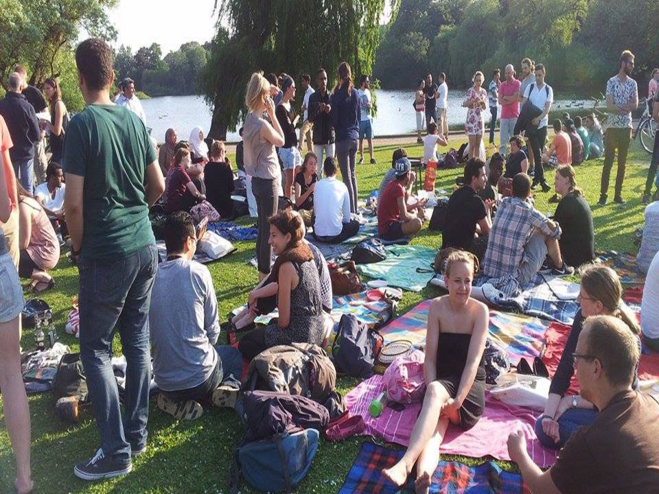 Eine kleine Menschenmenge hat es sich mit Sitzdecken in einem grünen Park gemütlich gemacht.