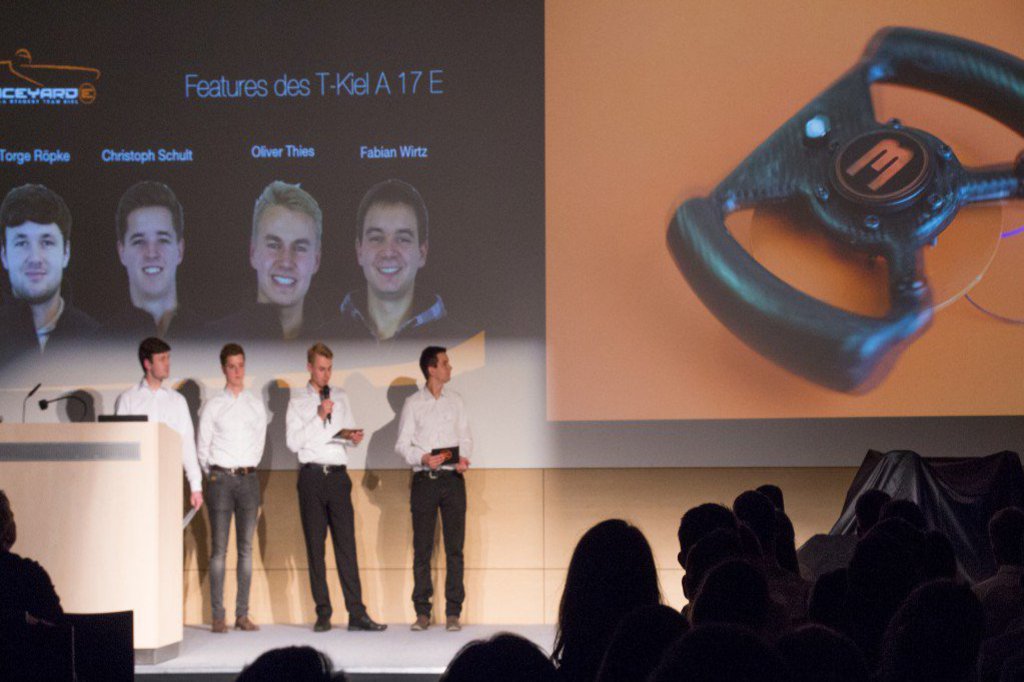 Ein aus 4 Männern bestehendes Team präsentiert die Merkmale eines Rennwagen.