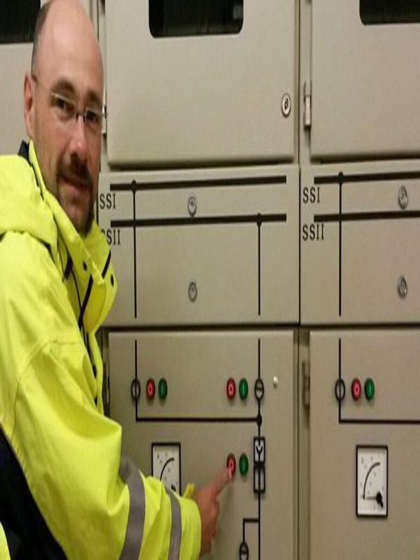 Ein Mann in gelber Warnjacke steht vor einem Schaltkasten und hält den Finger knapp über dem Hauptschalter der FH Kiel.