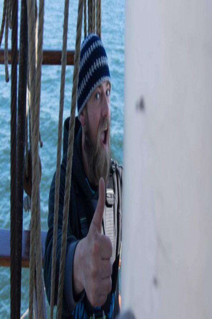 Ein mit Sicherheitsgurt ausgestatteter Mann streckt zwischen Tauen und Stricken den Daumen in die Kamera.