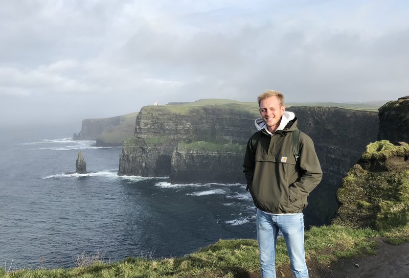 Tim steht vor einer Klippe mit dem Meer im Hintergrund