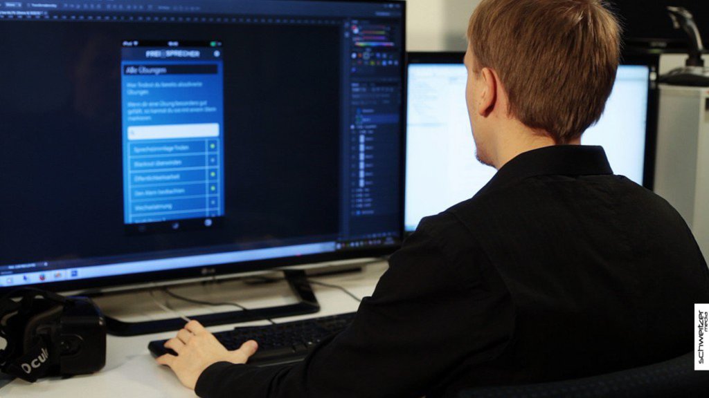 Ein Mann in schwarzem Pullover sitz vor einem Monitor und arbeitet an der Bedienoberfläche einer App.