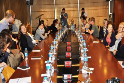 An einem großen hölzernen Konferenztisch sitzt eine gemischte Gruppe Studierender.