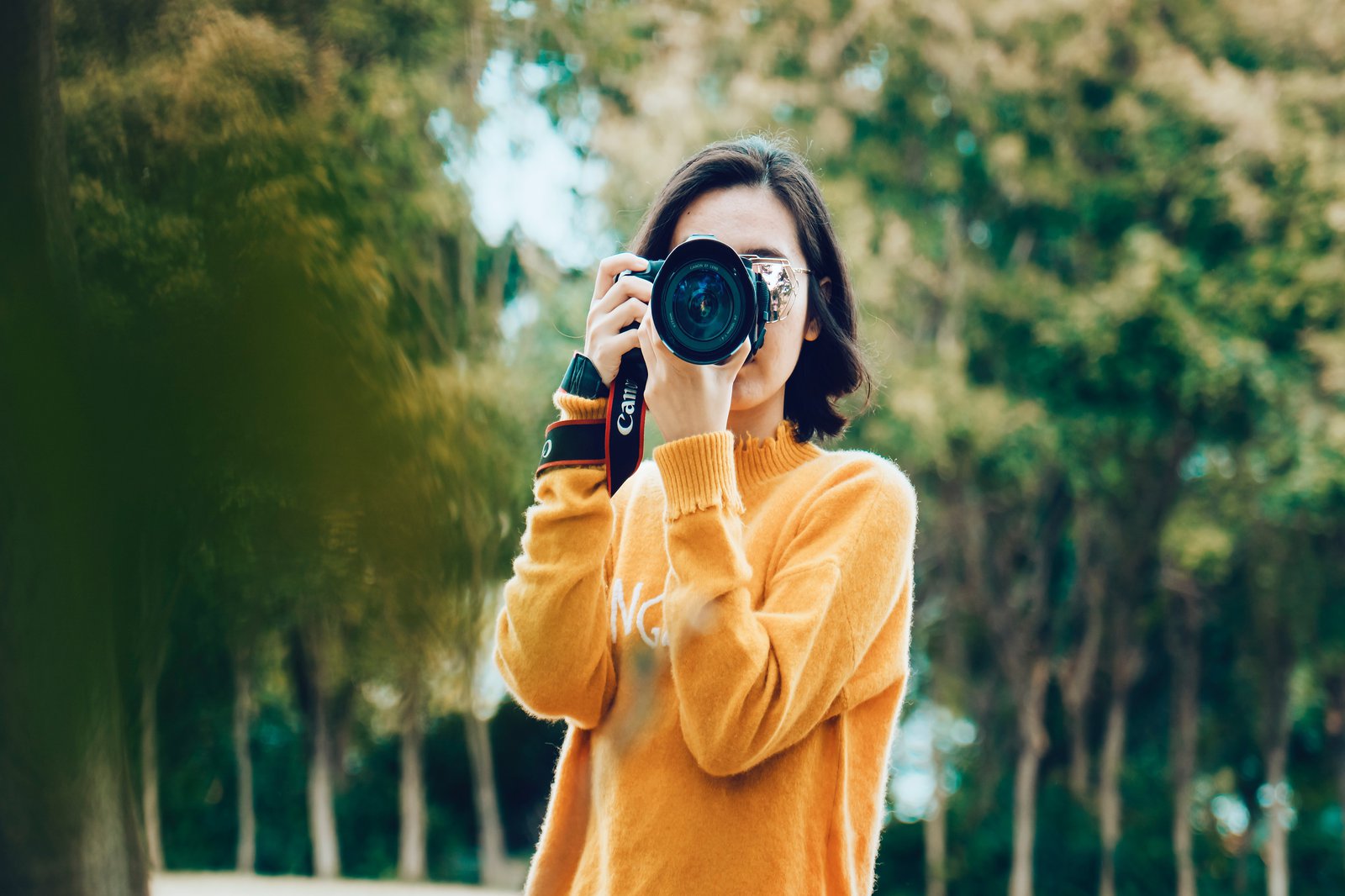 Eine Frau in orangenem Pullover hält eine Kamera um etwas zu fotografieren.