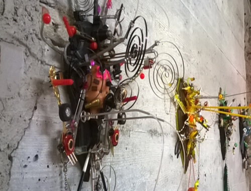 An einer weißen Betonwand hängen wilde Kunstwerke.