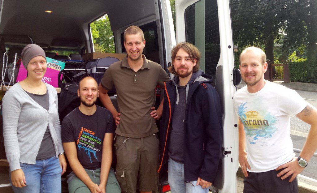 Eine Gruppe Studierender wartet vor einem voll bepacktem Van.