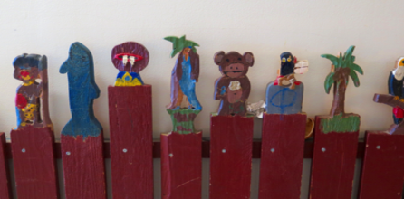 Die Spitzen, der Latten eines Zauns sind zu bunten Figuren geschnitzt und bemalt worden.