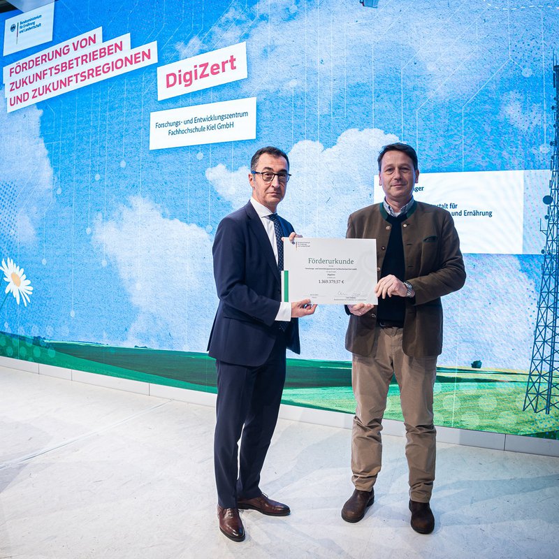 der ehemalige Bundeslandwirtschaftsminister Cem Özdemir (li.) übereicht Prof. Yves Reckleben den Fördebescheid für das Projekt DigiZert