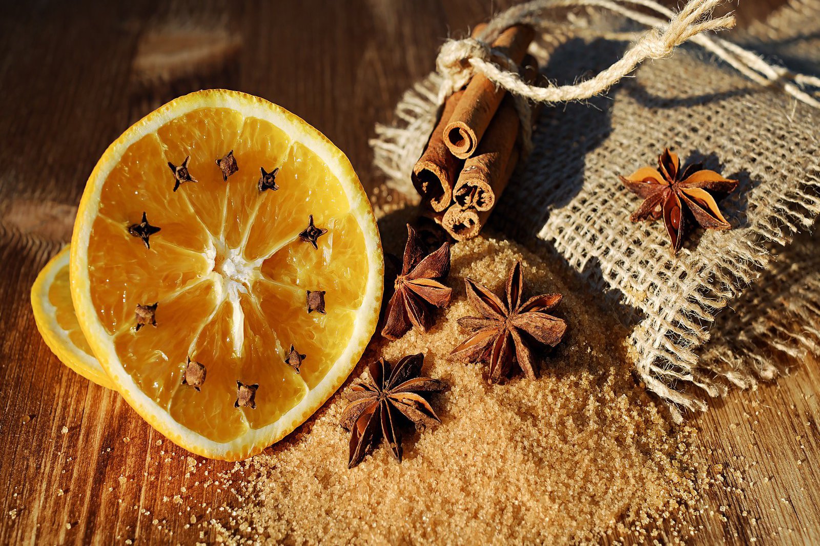 Ein Bund Zimtstangen, eine Orangenscheibe und Nelken umgeben einen Haufen braunen Zucker.