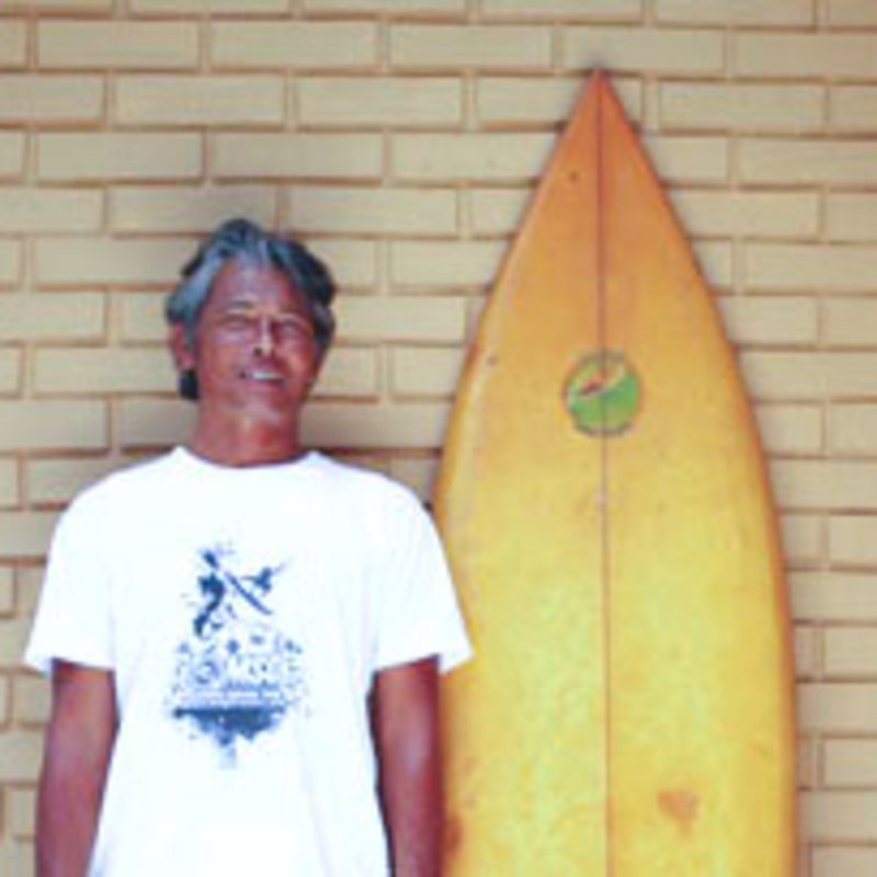 Ein Mann in weißem T-Shirt, steht neben seinem gelben Surfbrett.