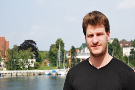 Ein Mann in schwarzem T-Shirt, lächelt Nahe der Schwentinemündung in die Kamera.