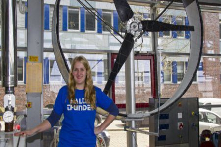 Eine Studentin steht in einer Halle, neben ihr ein großer Propeller.