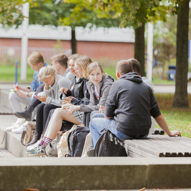 Junge Menschen auf dem Campus der Fachhochschule Kiel sitzen in der Sonne.