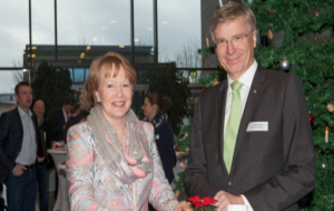 Eine festlich gekleidete Frau und ein Mann in Anzug, posieren an einem Stehtisch für die Kamera.