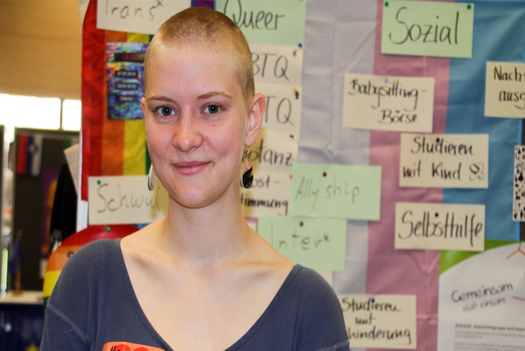 Eine Frau posiert vor einem Plakat und lächelt in die Kamera.