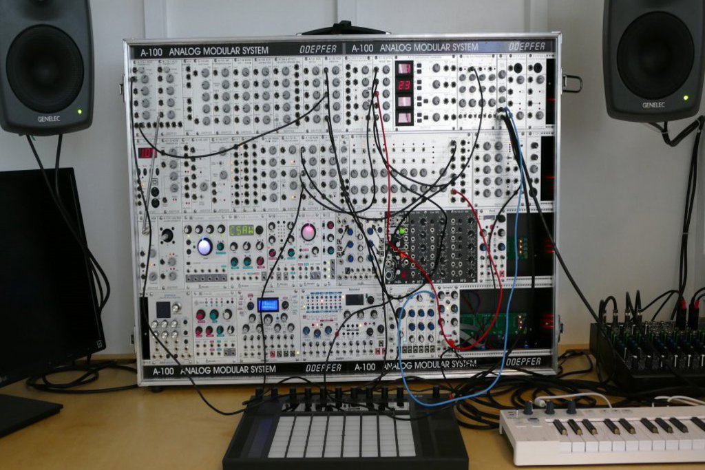 Ein Schaltkasten umgeben von 2 Keyboards, Boxen und einem Mischpult.