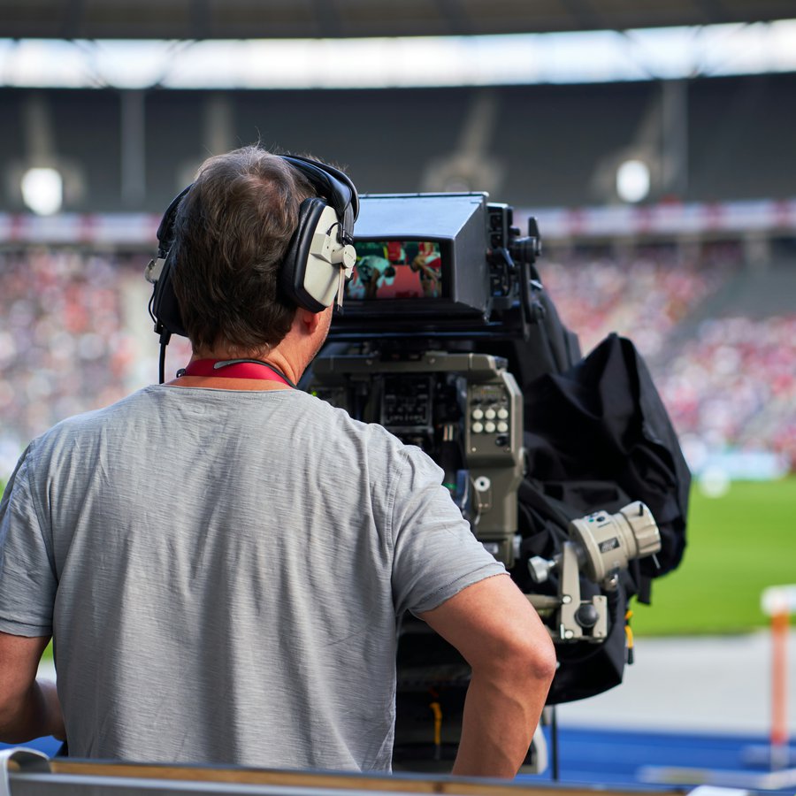 Ein Mann bedient eine große Kamera in einem Fußballstadion.