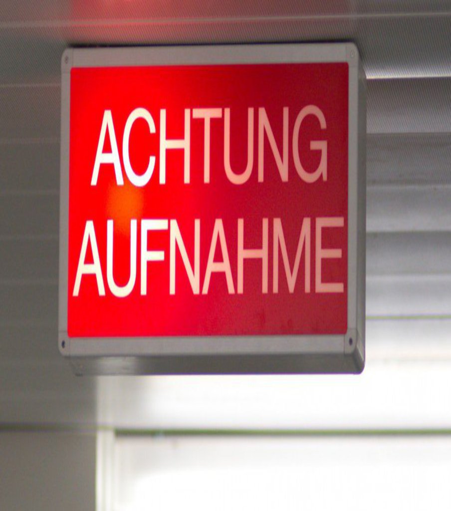 Von der Decke eines Weißen Flurs hängt ein Schild mit der Aufschrift "Achtung Aufnahme".