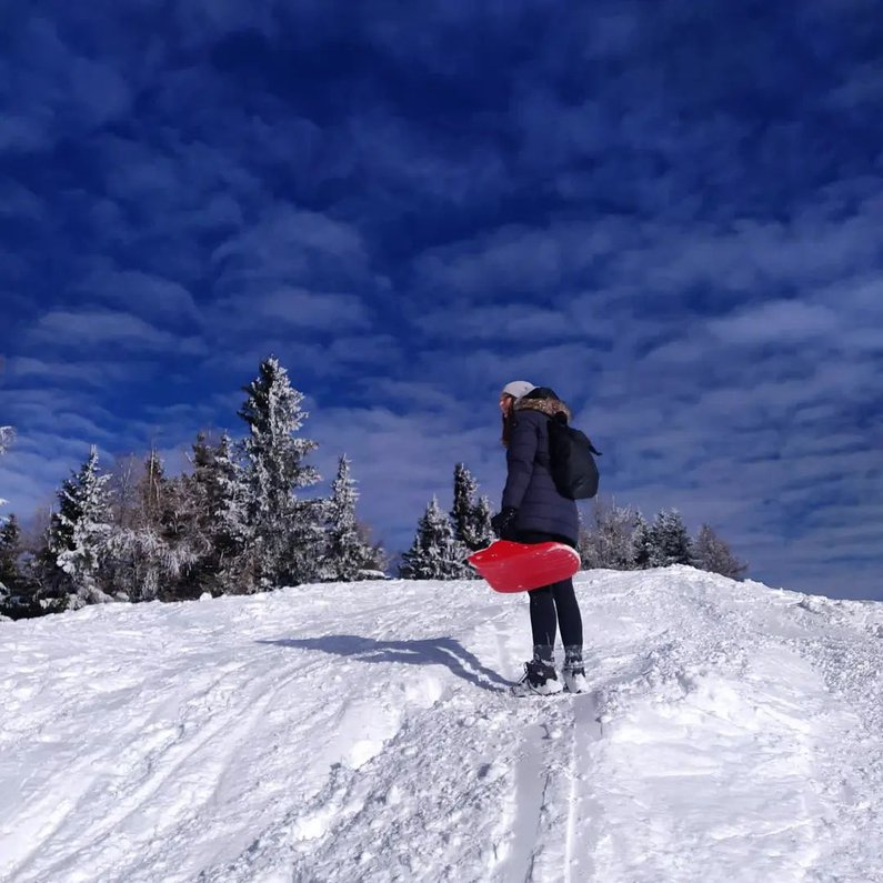 Jana steht auf einem verschneiten Berg und ist bereit zum Rodeln
